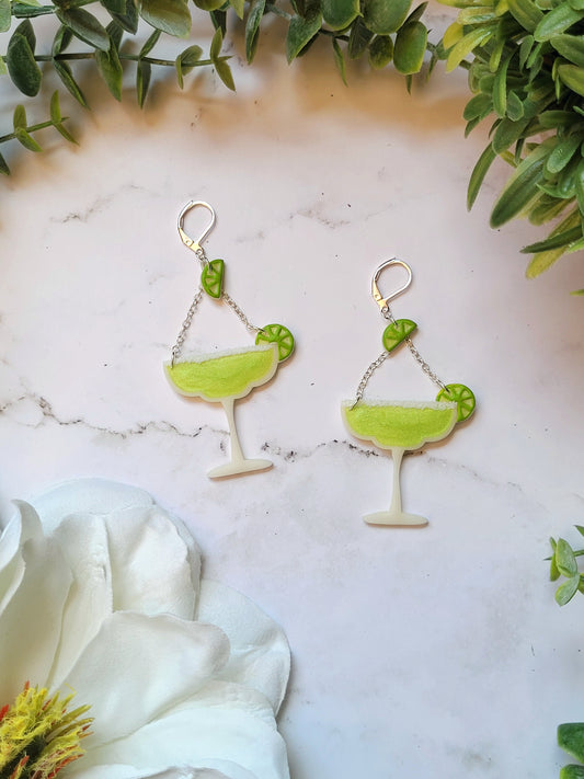 close up of Lime margarita glass earrings on a marble background with foliage.