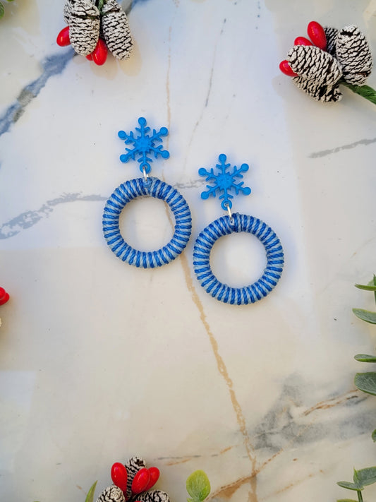 close up of snowflake striped hoop earrings on a white marble background surrounded by foliage.