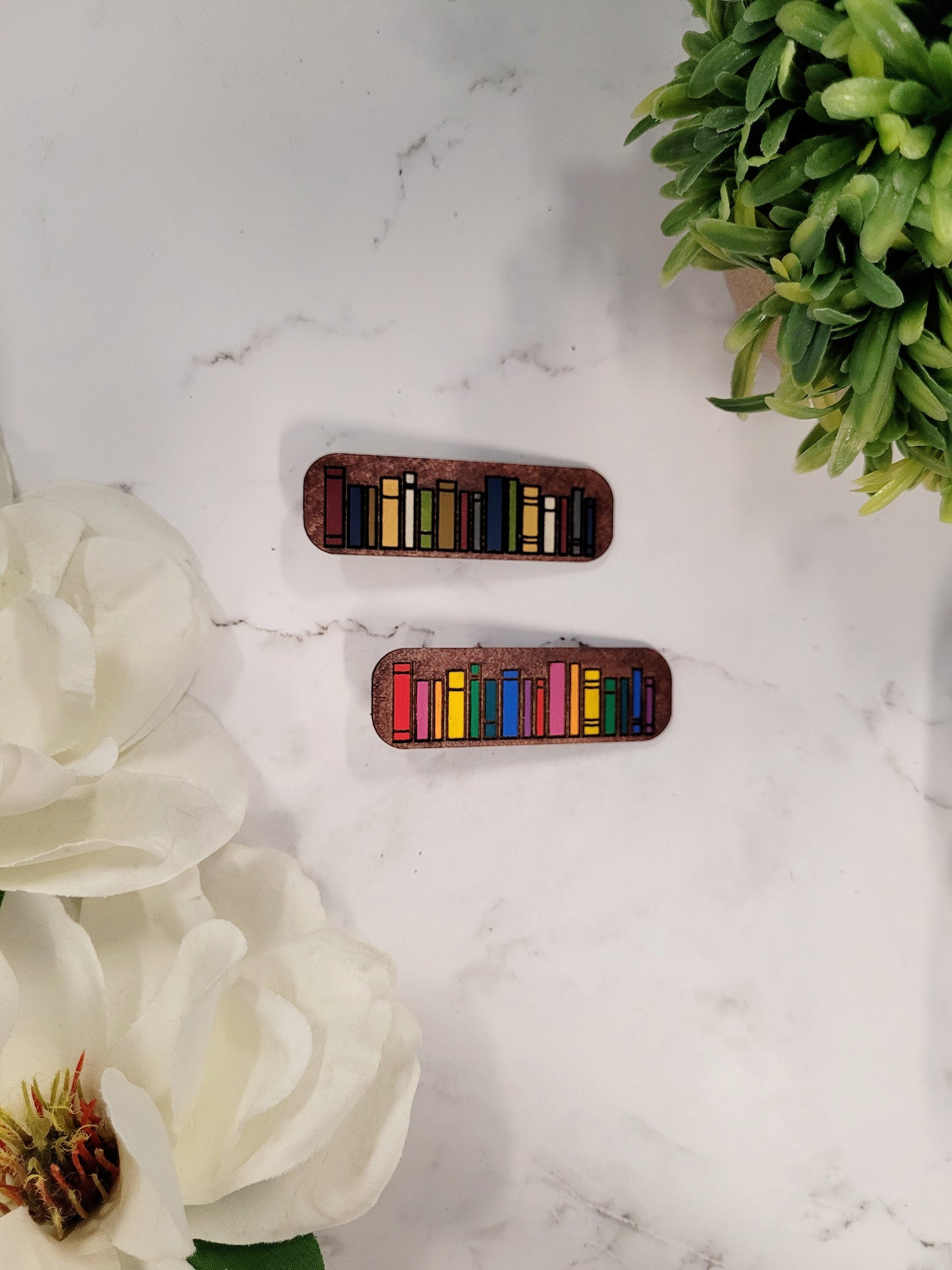 Book hair clips on a white marble background surrounded by foliage.