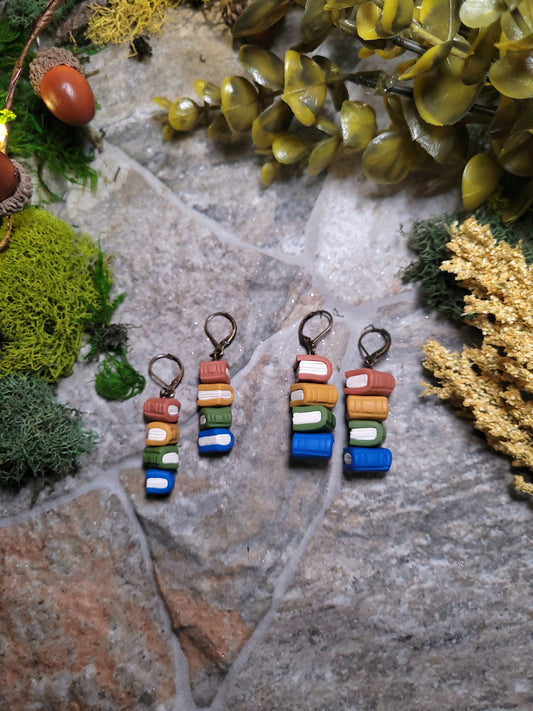Cottagecore bookstack earrings on a stone background surrounded by moss and foliage.