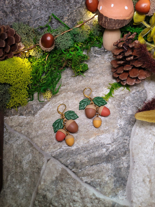 3d acorn shaped earrings with  oak leaves. Sitting on a stone background surrounded by foliage.