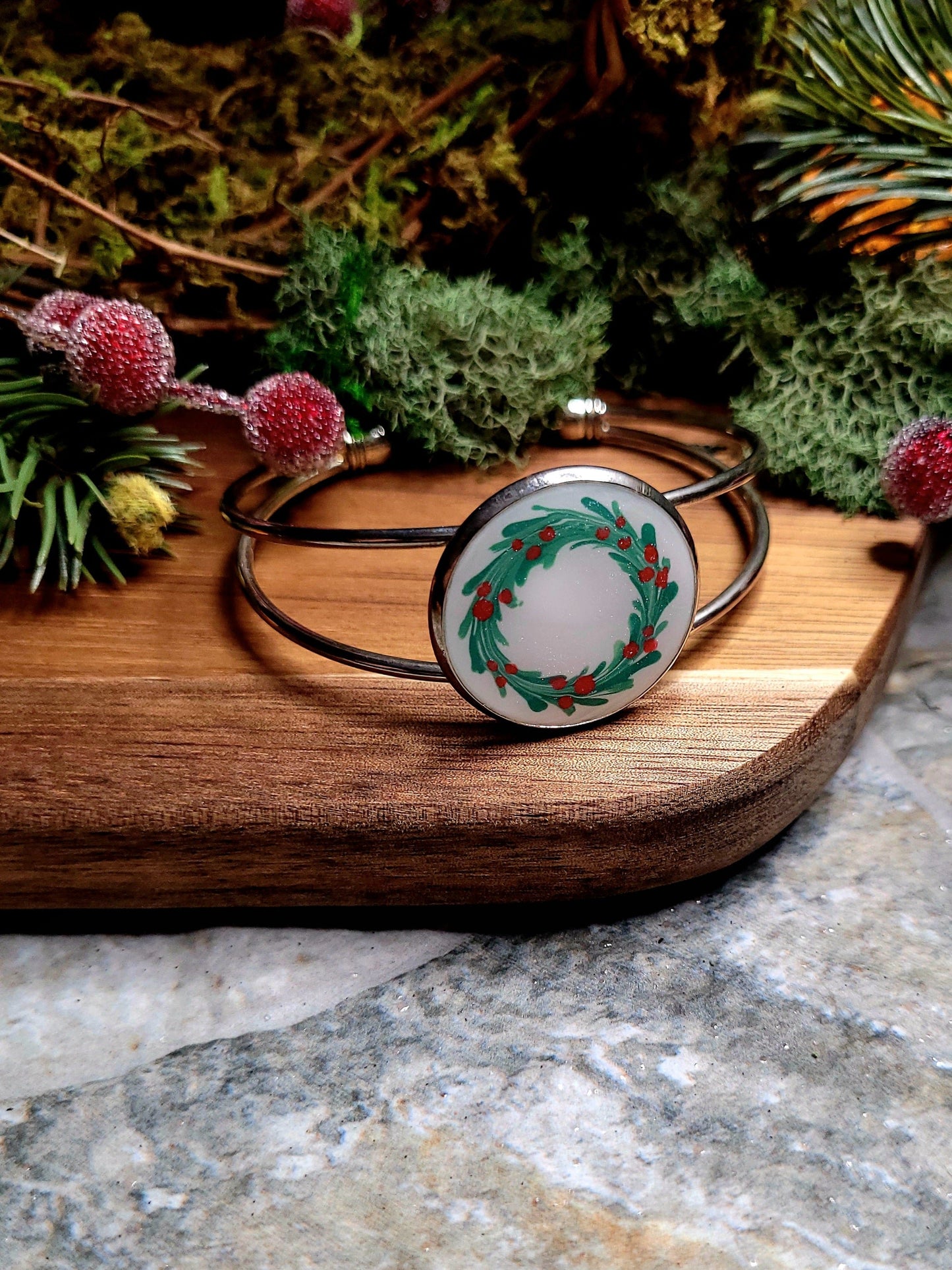 silver holly bracelet on a wood and stone background surrounded by foliage.