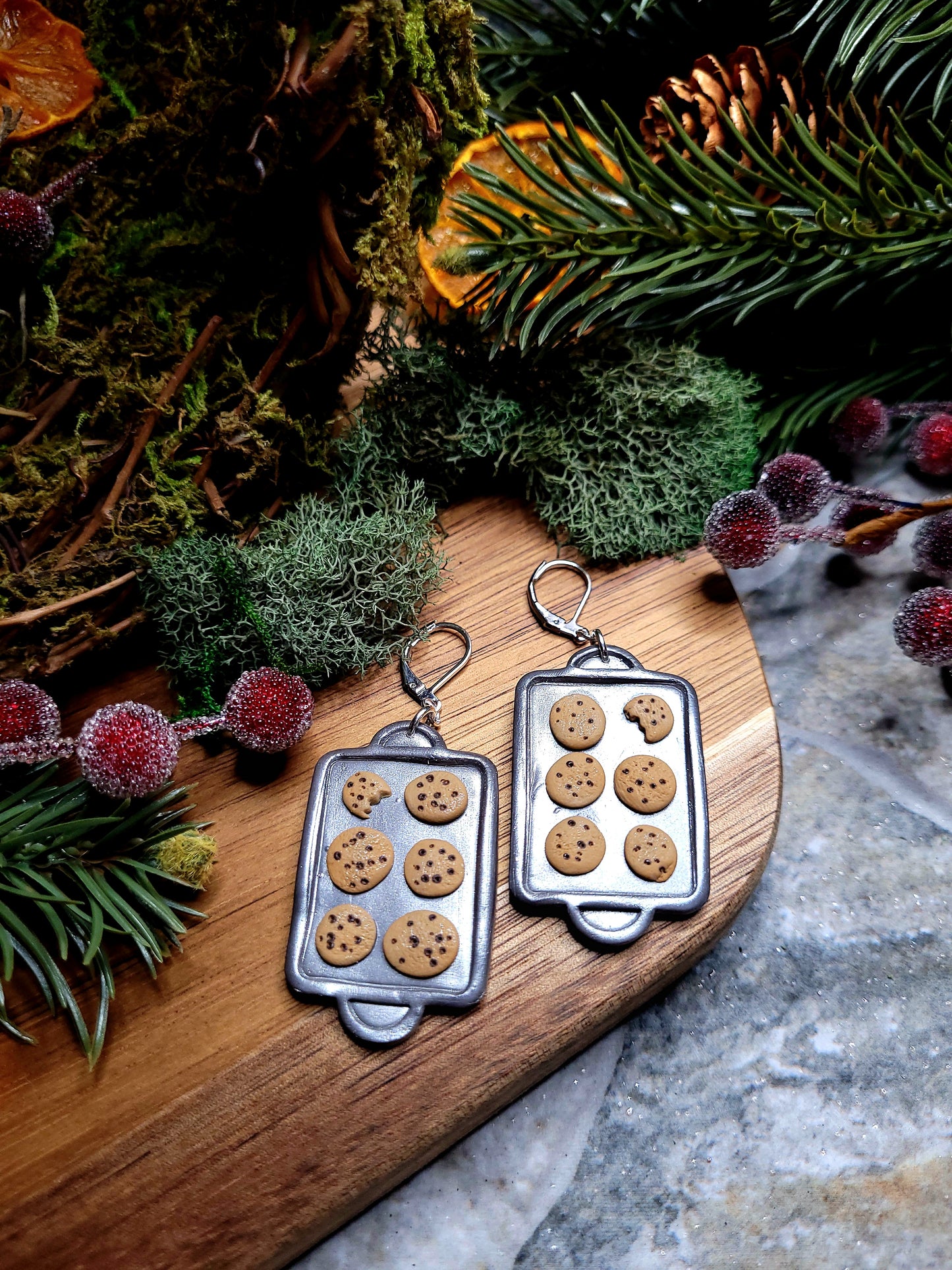 Cookie Tray earrings on a wood and stone background surrounded by foliage