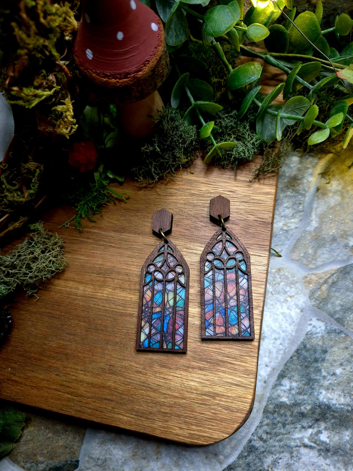 Autumn Cathedral window earrings on a stone background surrounded by foliage.