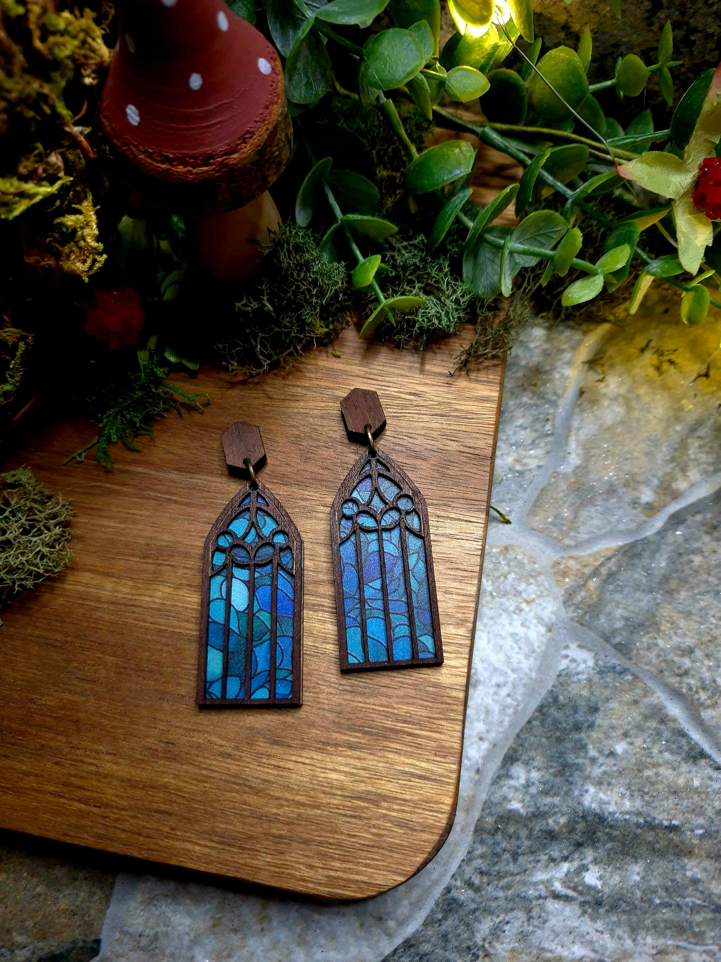 Ocean Cathedral window earrings on a wood and stone background surrounded by foliage.