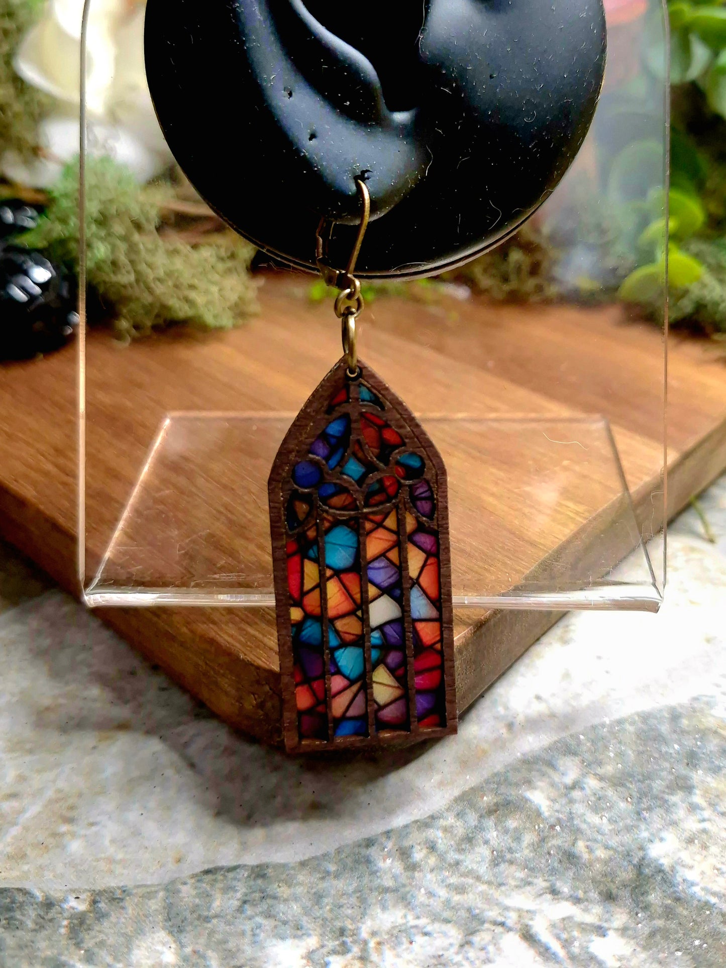 Jewel Cathedral window earrings on a display ear on a wood and stone background