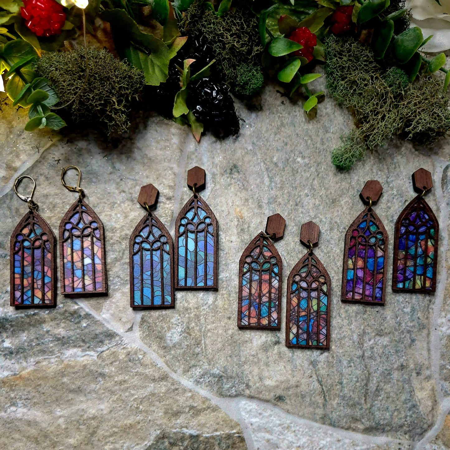 4 colors of Cathedral window earrings on a stone background surrounded by foliage.