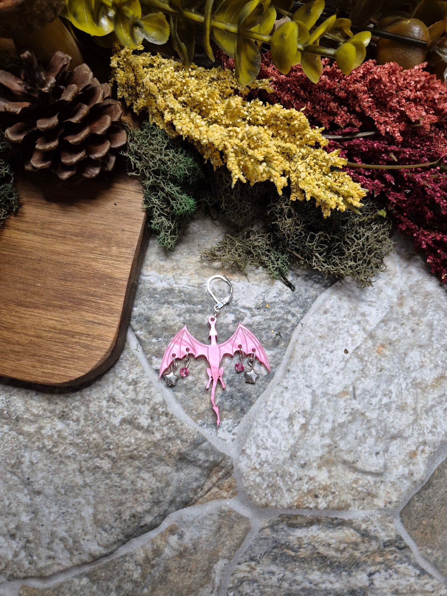pink dragon dangle on a stone background surrounded by foliage.