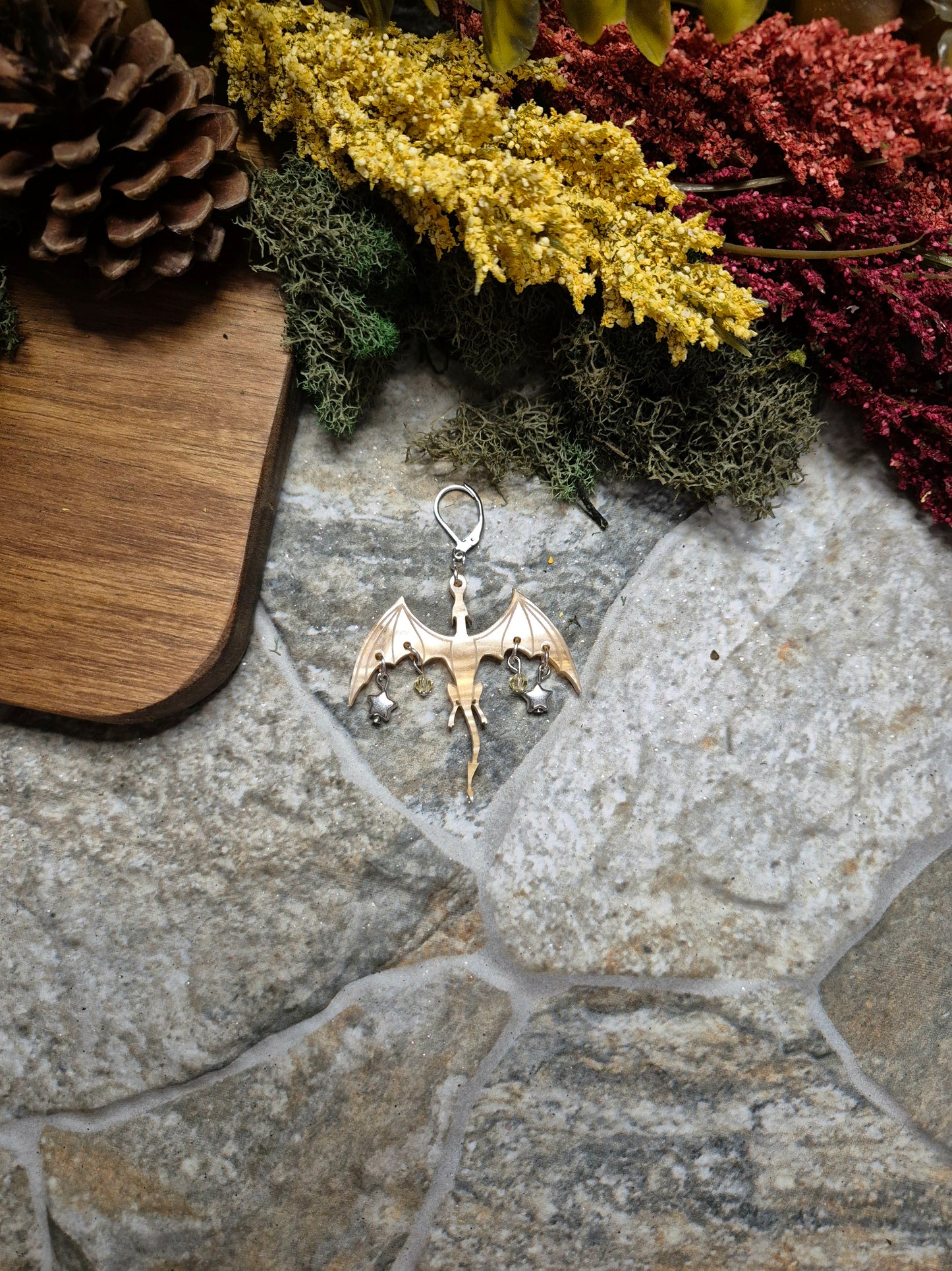 gold dragon dangle on a stone background surrounded by foliage.