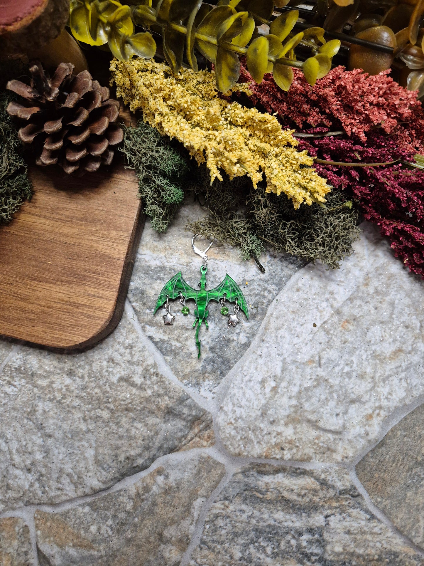 green dragon dangle on a stone background surrounded by foliage.