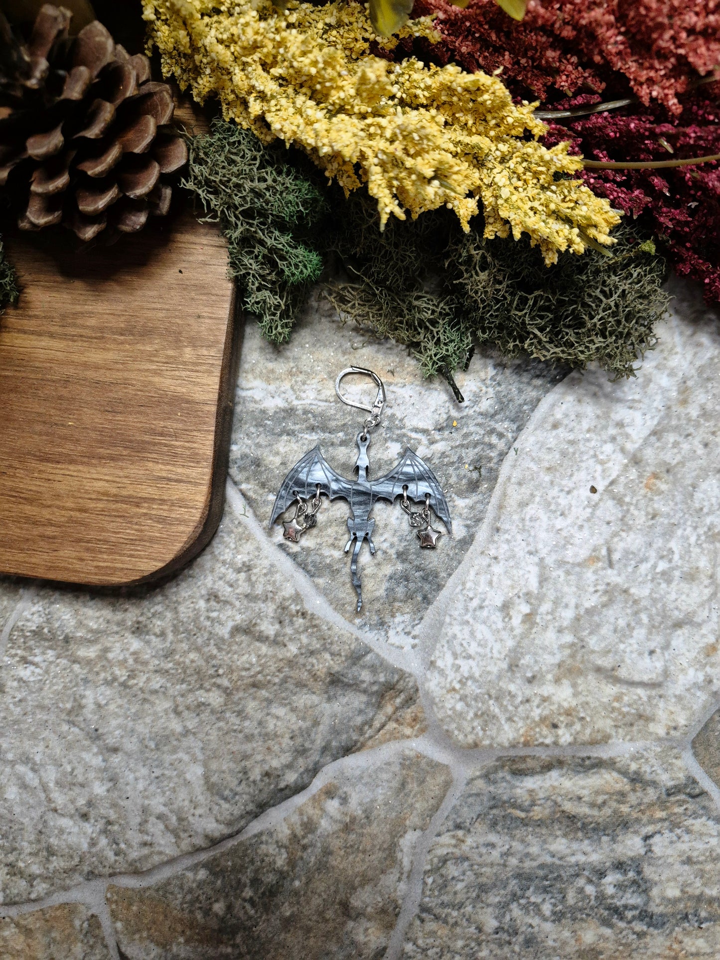 silver dragon dangle on a stone background surrounded by foliage.