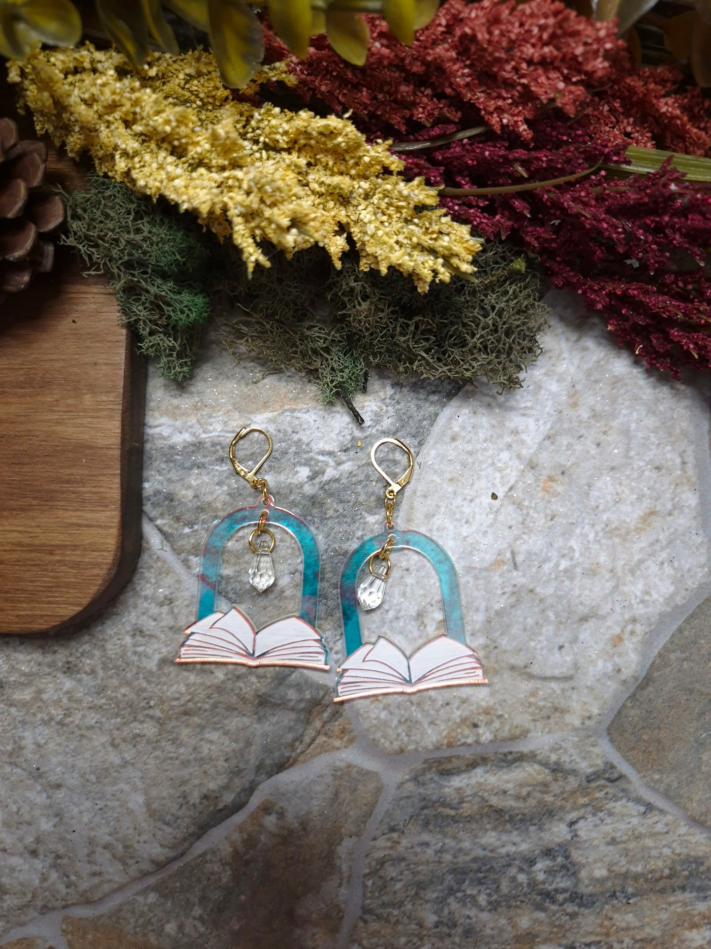 Open Book Arch earrings on a stone background surrounded by foliage