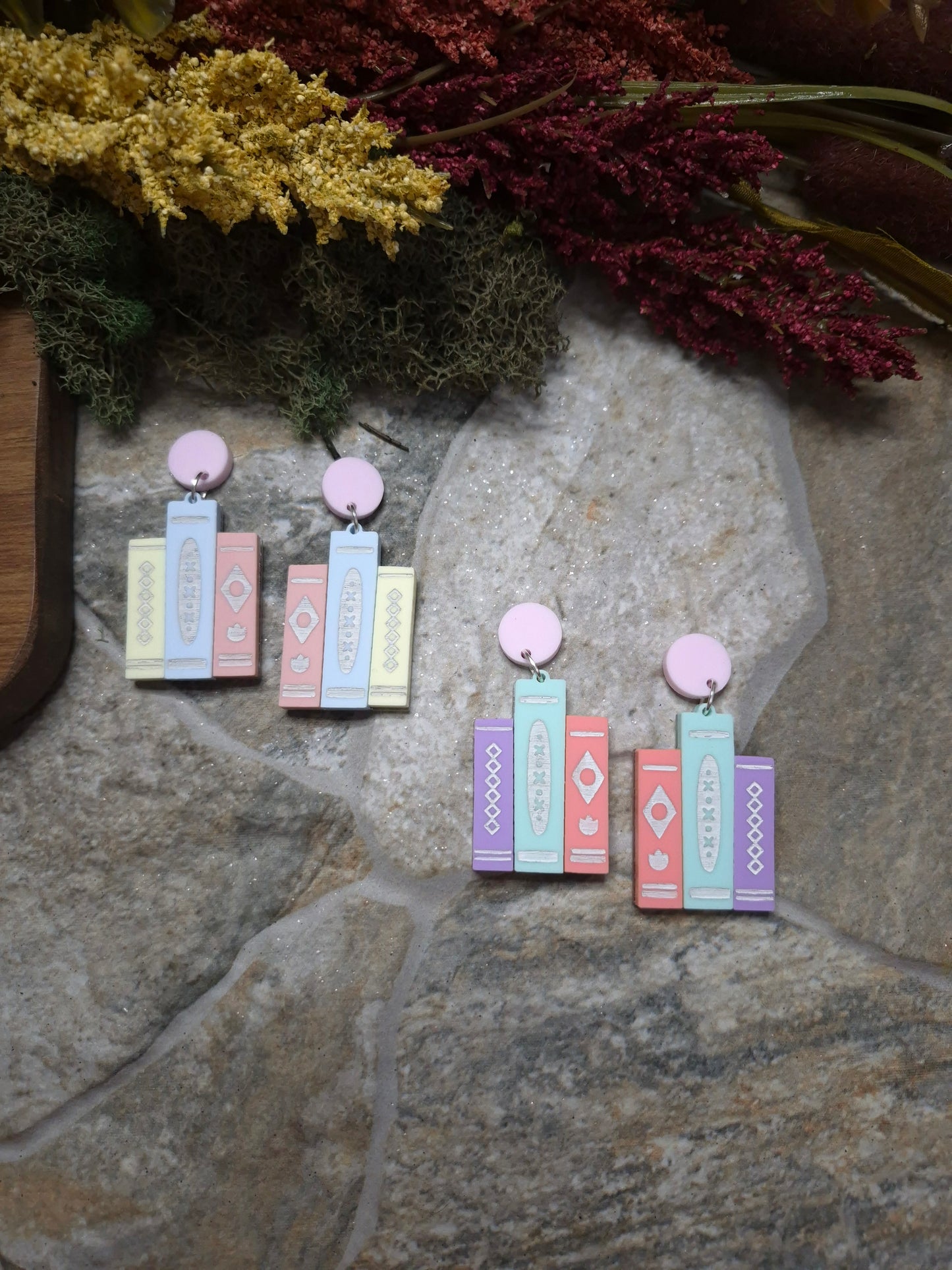 2 colorways of retro book earrings on a stone background surrounded by foliage