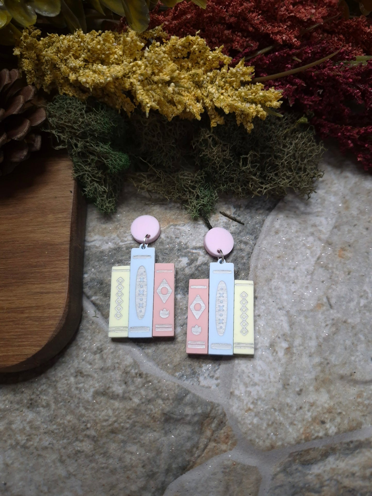 Pastel retro book earrings on a stone background surrounded by foliage