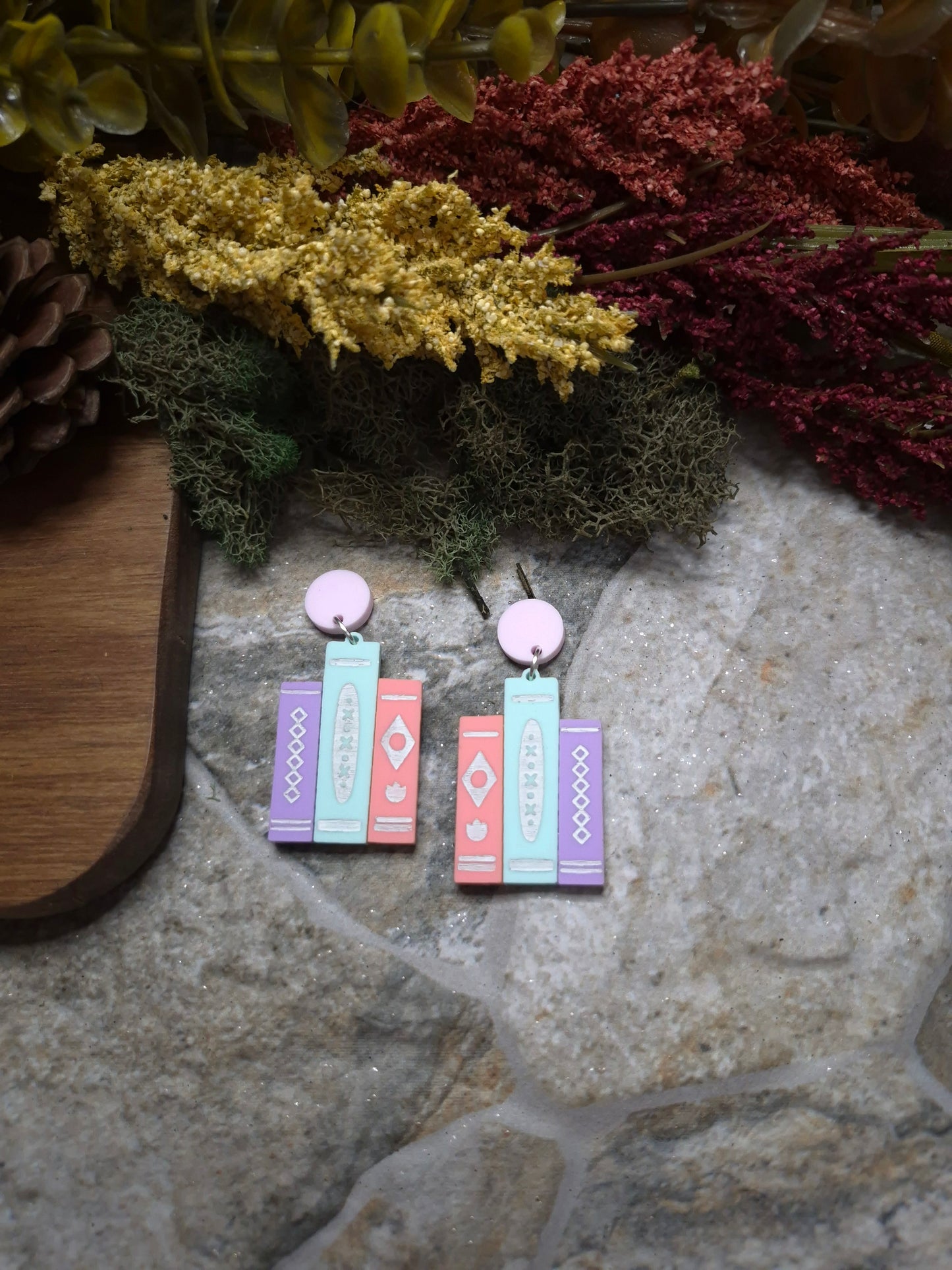 Vibrant retro book earrings on a stone background surrounded by foliage