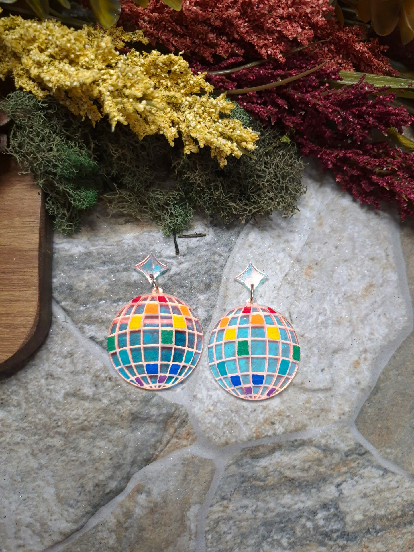 close up of Colorful disco ball earrings on a stone surface with decorative plants.