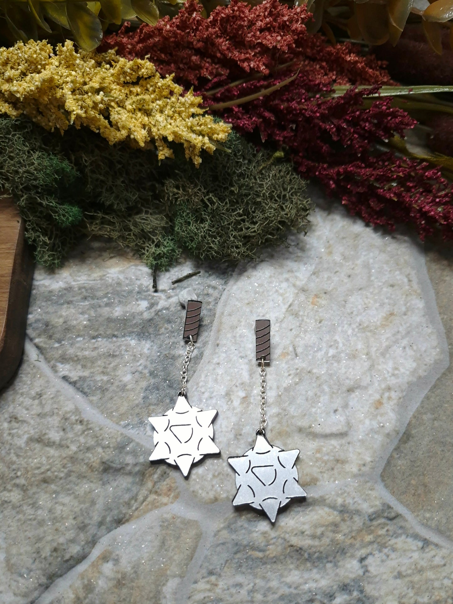 flail earrings on a stone background surrounded by foliage.