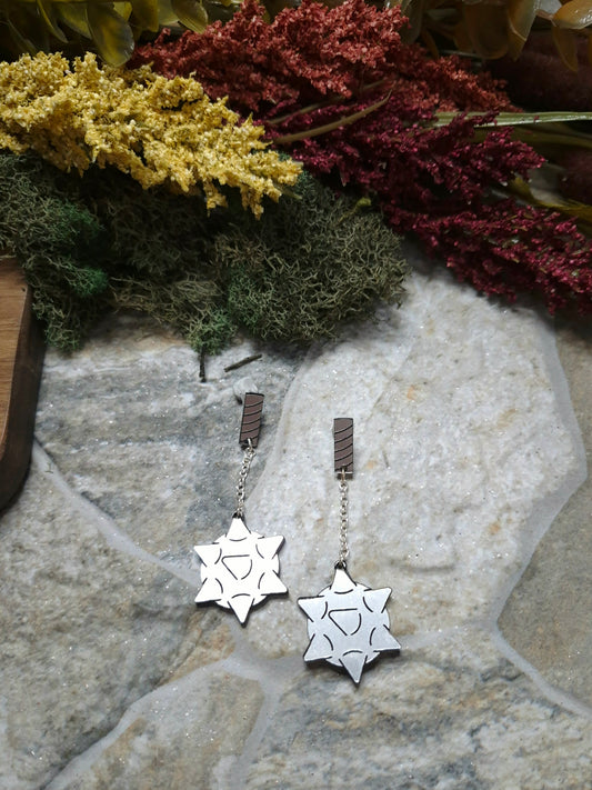 flail earrings on a stone background surrounded by foliage.