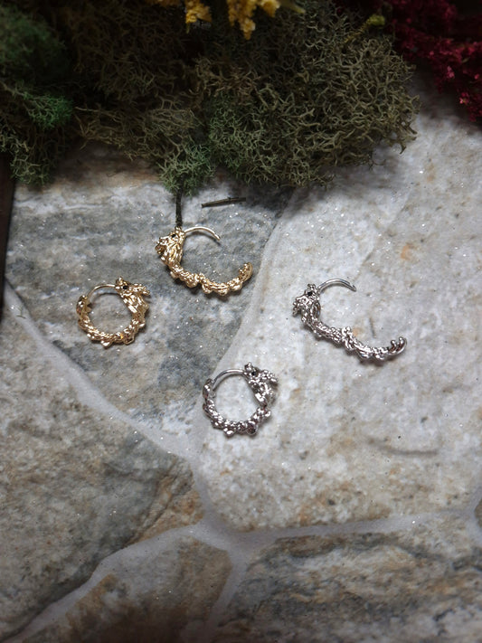 Gold and Silver dragon hoop earrings open and closed on a stone background surrounded by foliage
