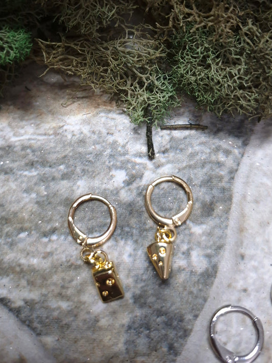 Gold cheese wedge earrings on a stone background surrounded by foliage