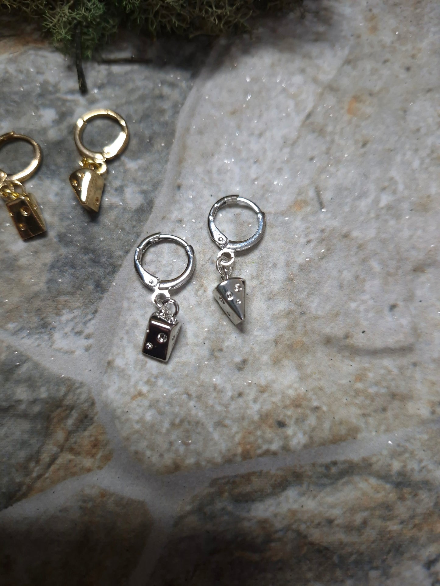 Silver cheese wedge earrings on a stone background surrounded by foliage