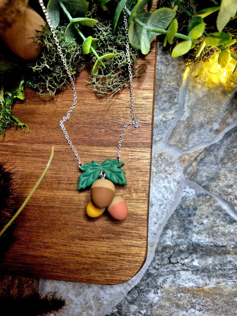 Acorn Necklace on a wood and stone background surrounded by foliage