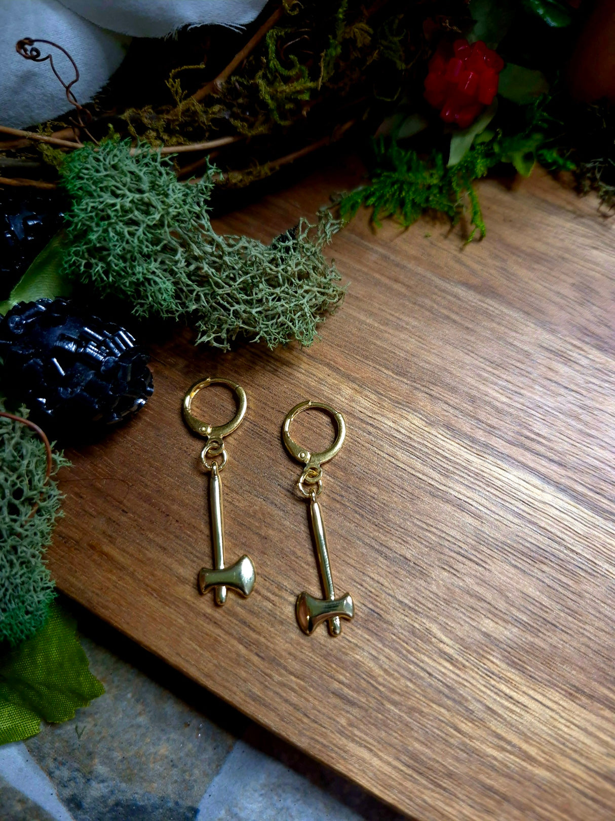 Gold Axe Earrings on a wood and stone background surrounded by foliage