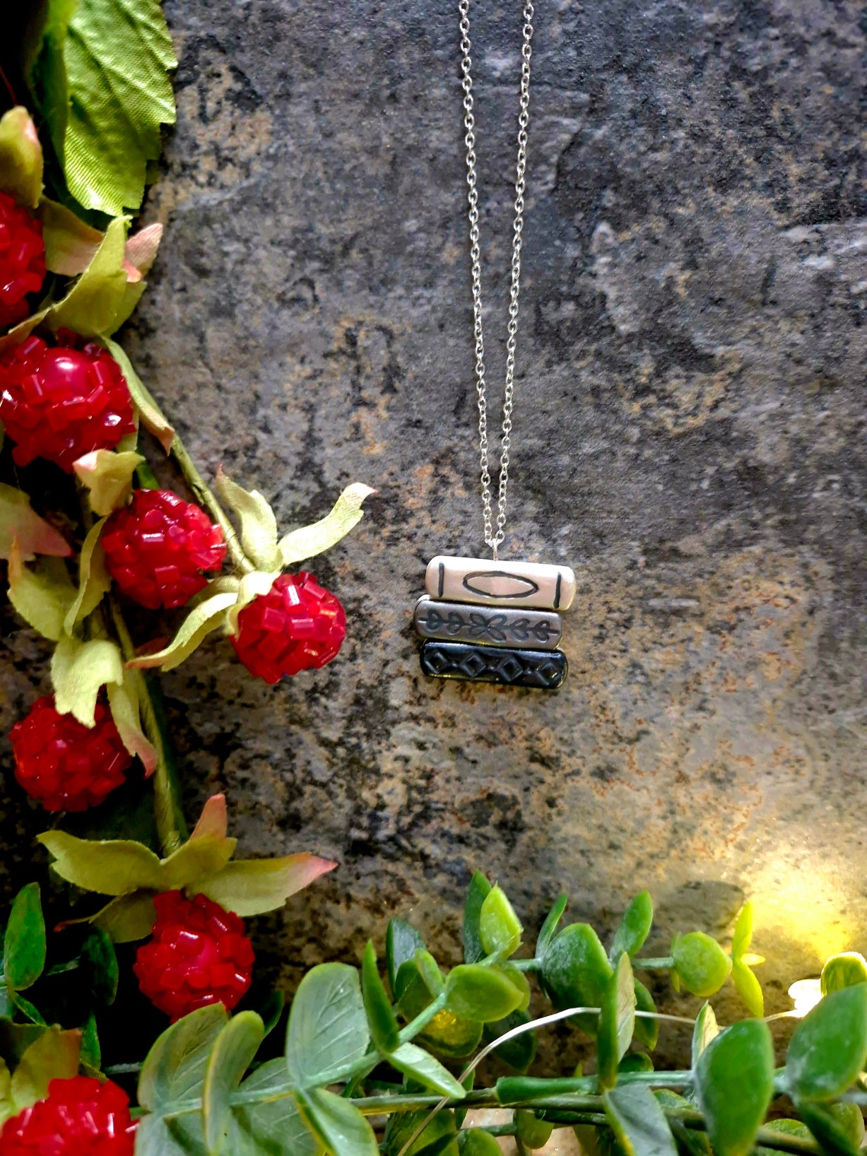 greyscale bookstack necklace on a  stone background surrounded by foliage