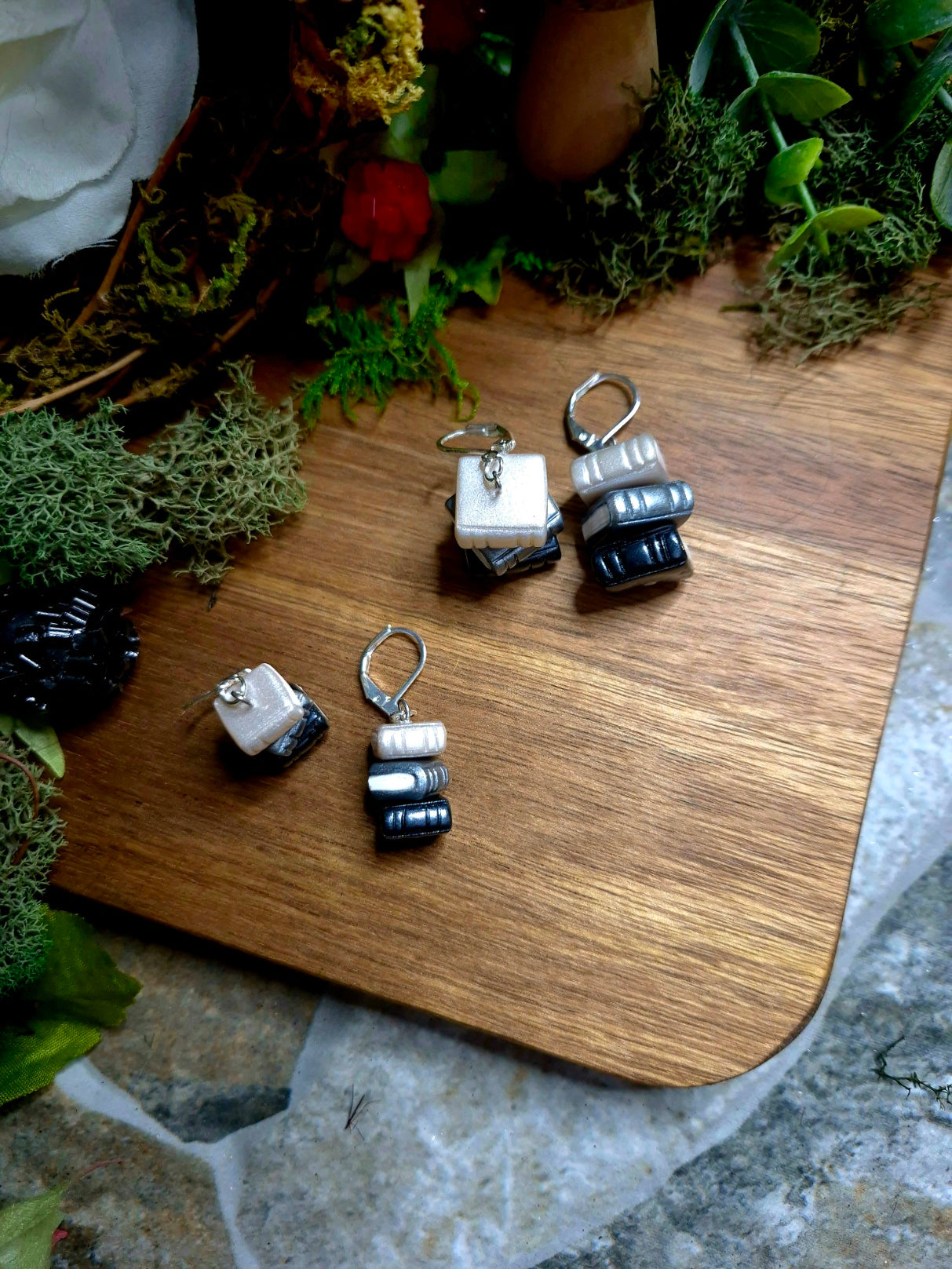 Regular and Mini greyscale bookstack earrings on a wood and stone background surrounded by foliage