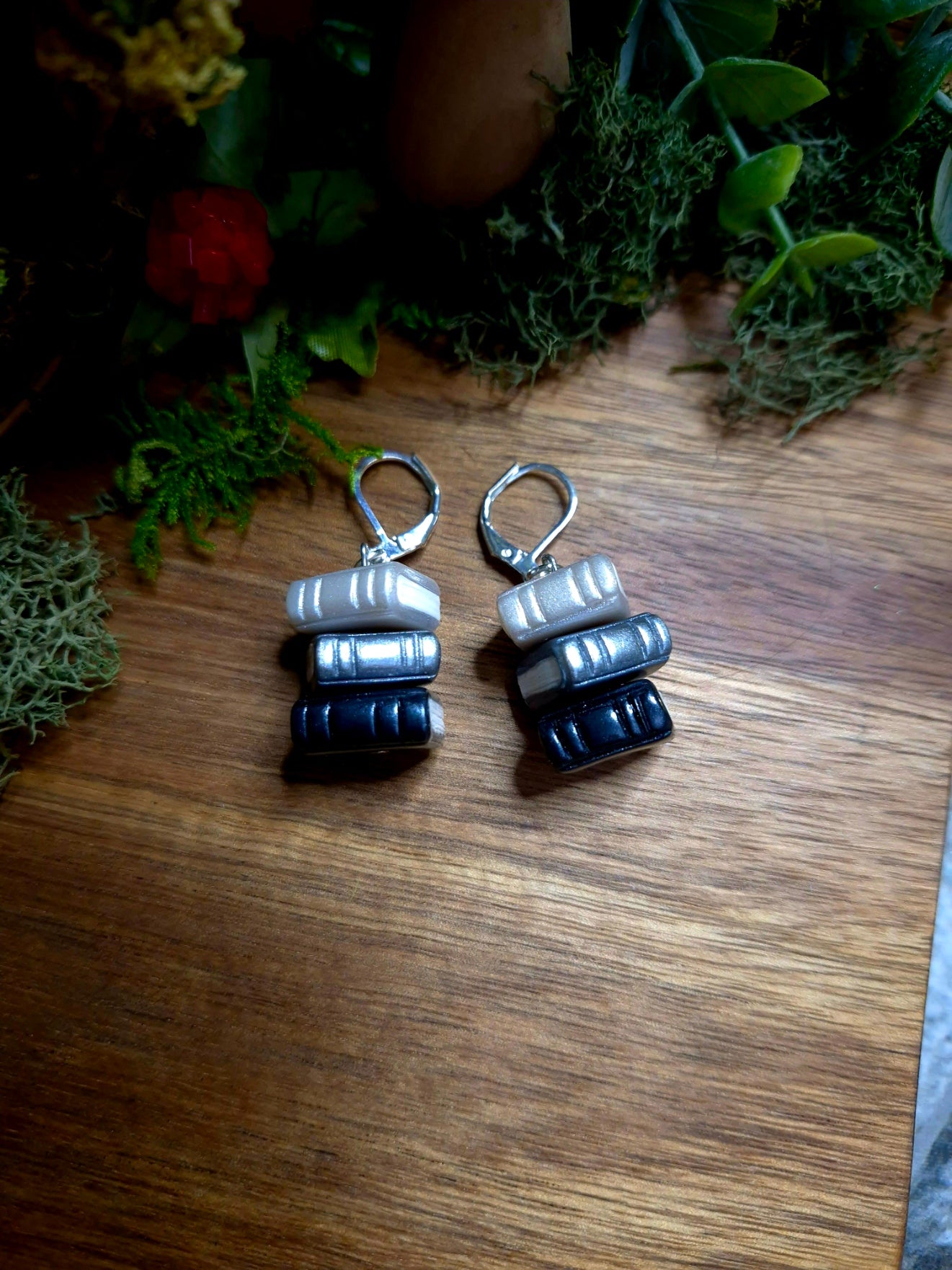 Regular greyscale bookstack earrings on a wood and stone background surrounded by foliage