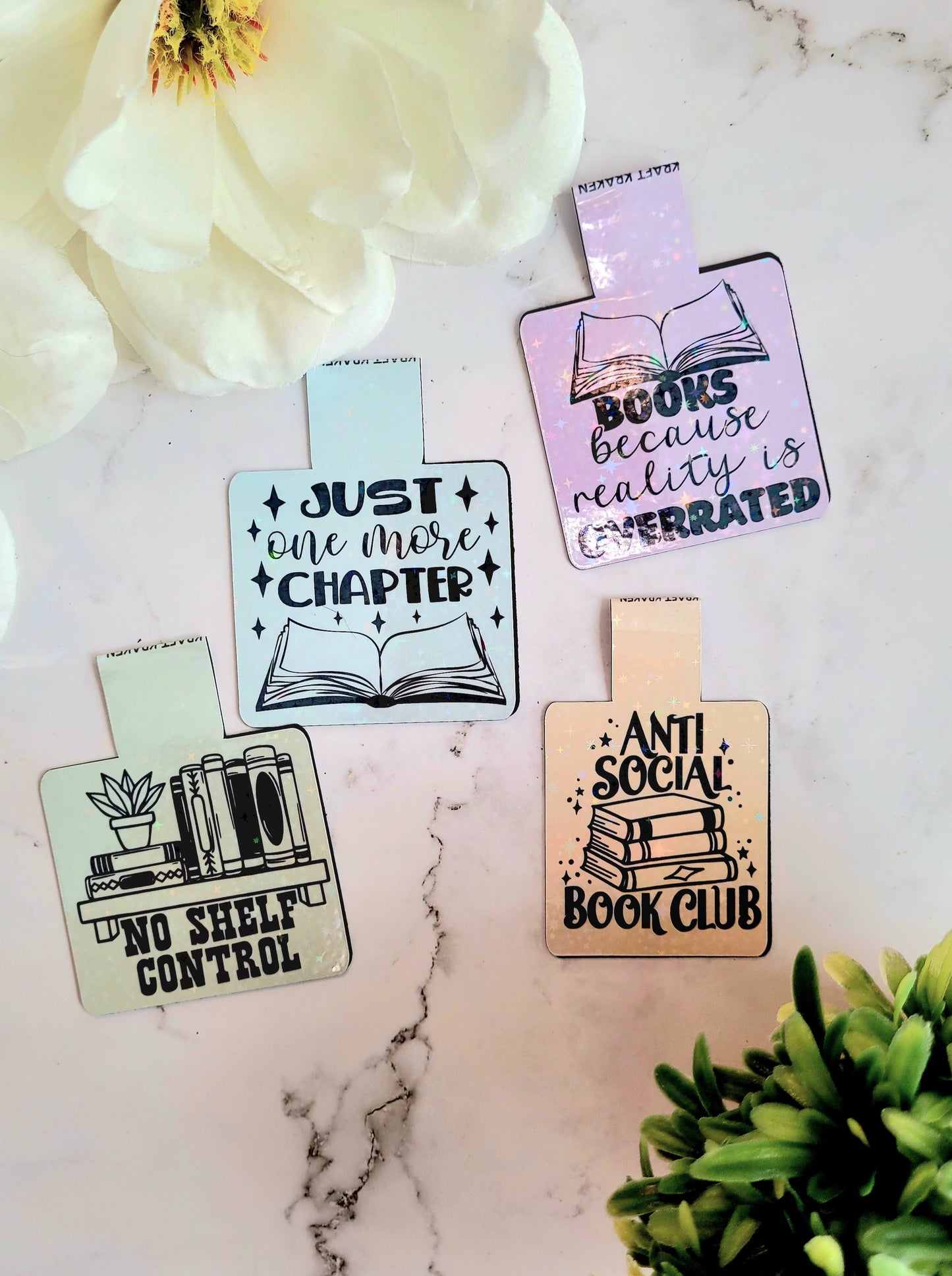 shelf control, one more chapter, reality, anti-social bookmarks on a marble background surrounded by foliage.