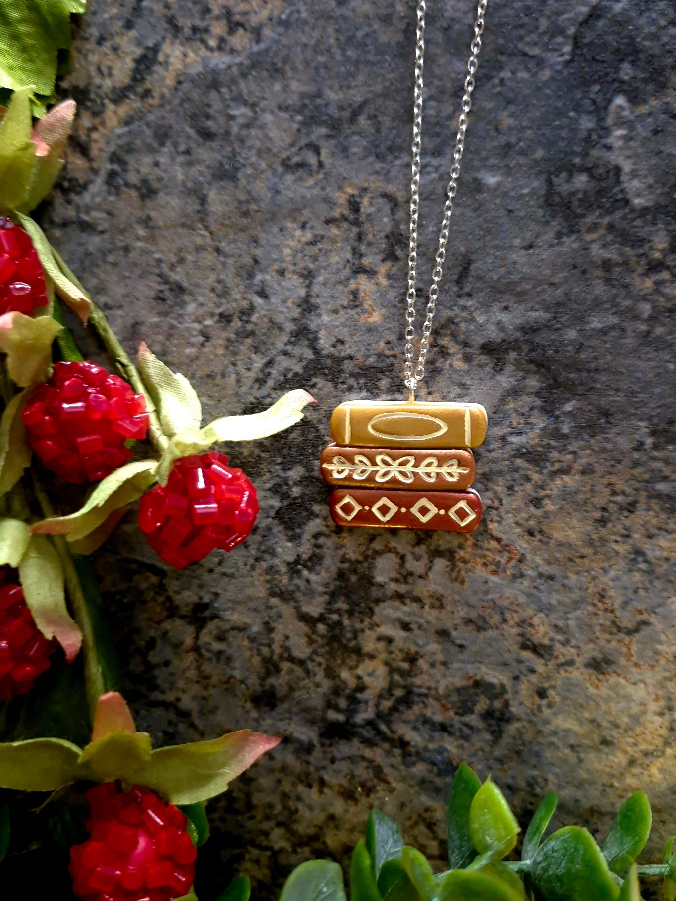 Copper bookstack necklace on a stone background surrounded by foliage
