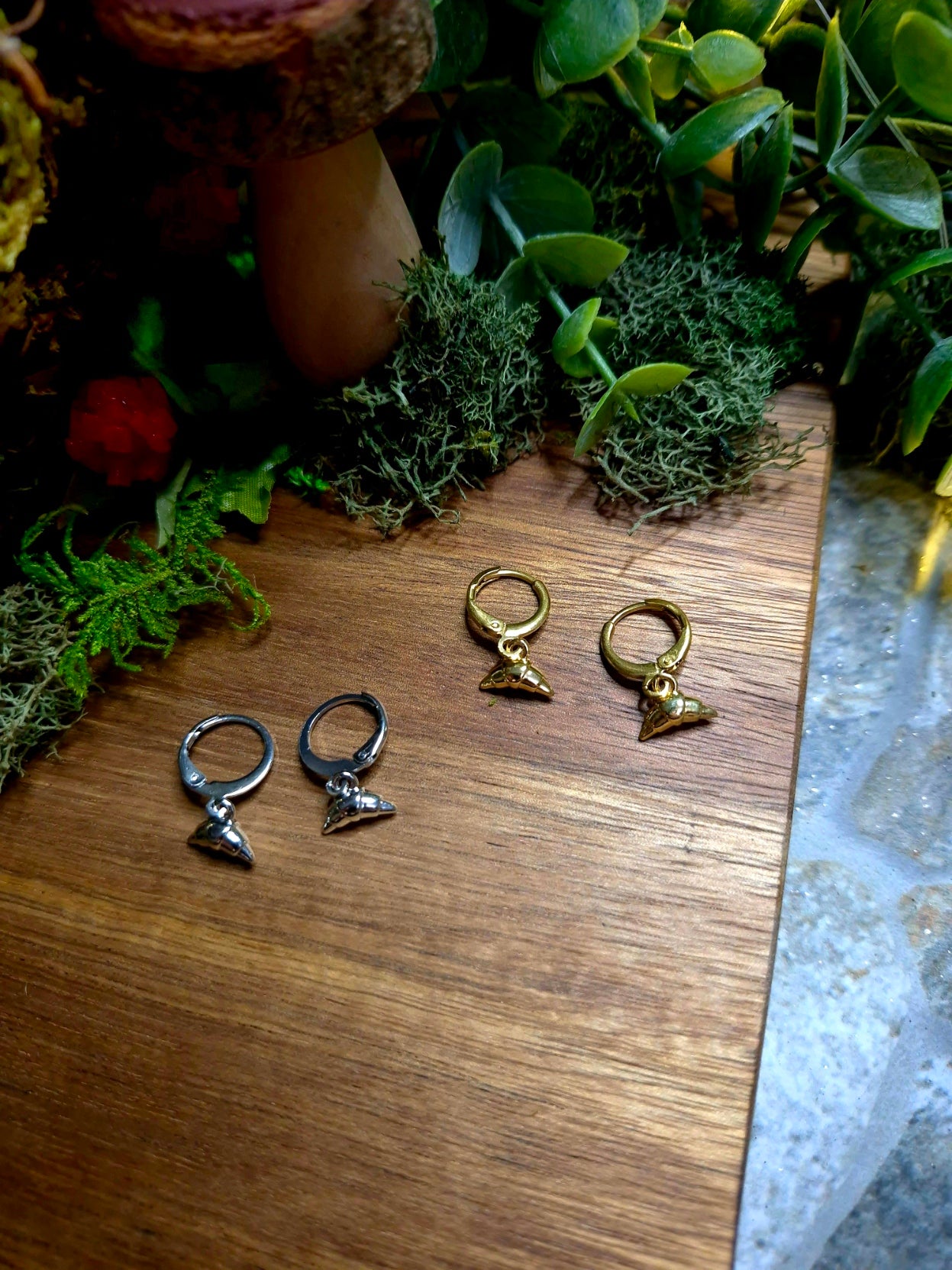 gold and silver croissant charm earrings on wood and stone background