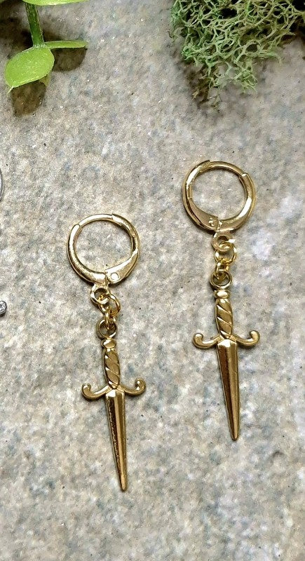 gold dagger earrings on a stone background.