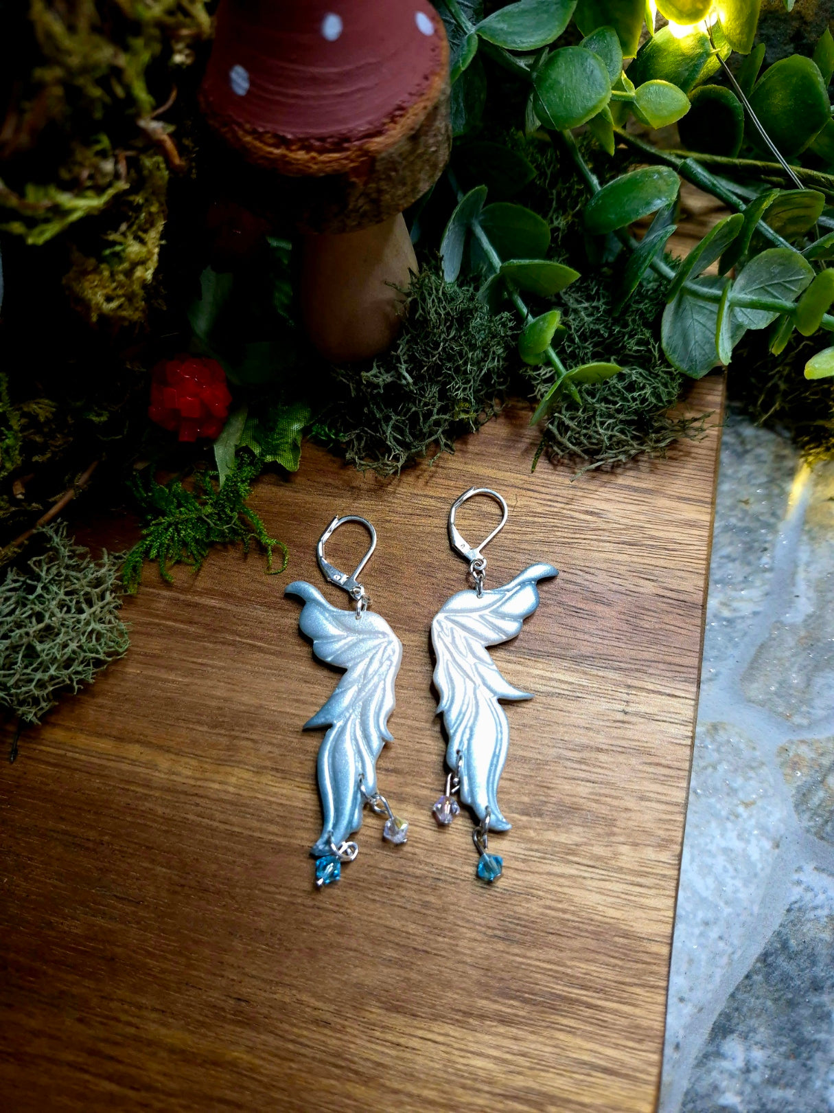 blue fairy wing earrings on a wood and stone background