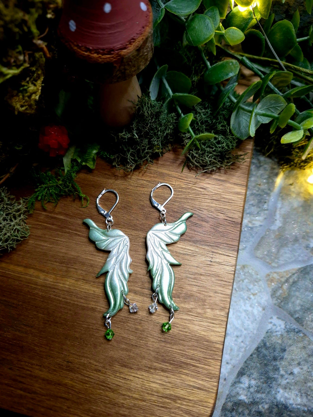 green fairy wing earrings on a wood and stone background