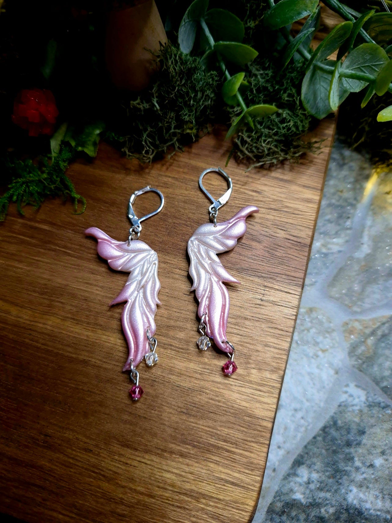 Pink fairy wing earrings on a wood and stone background