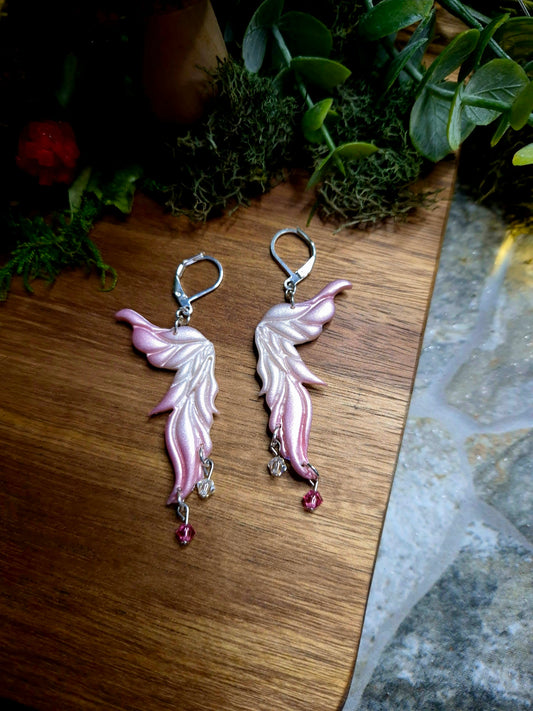 Pink fairy wing earrings on a wood and stone background