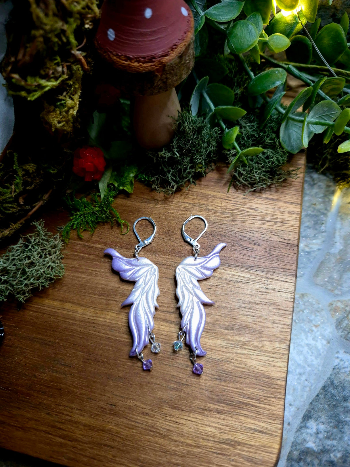 purple fairy wing earrings on a wood and stone background