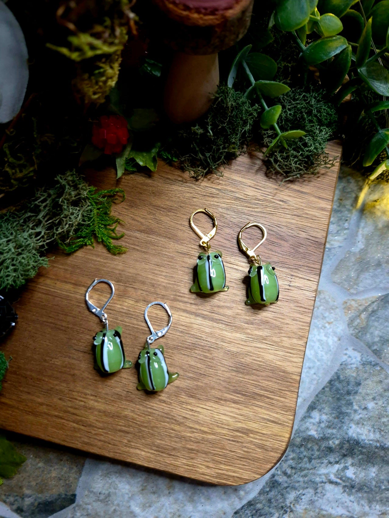 Gold and silver frog charm earrings on a wood and stone background