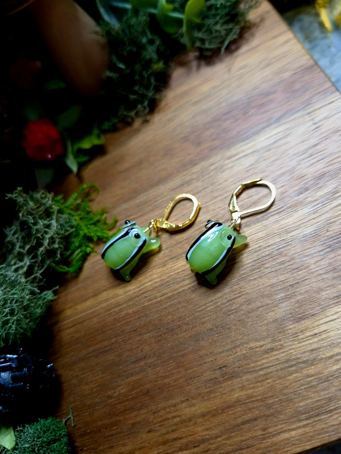 gold frog charm earrings on a wood and stone background