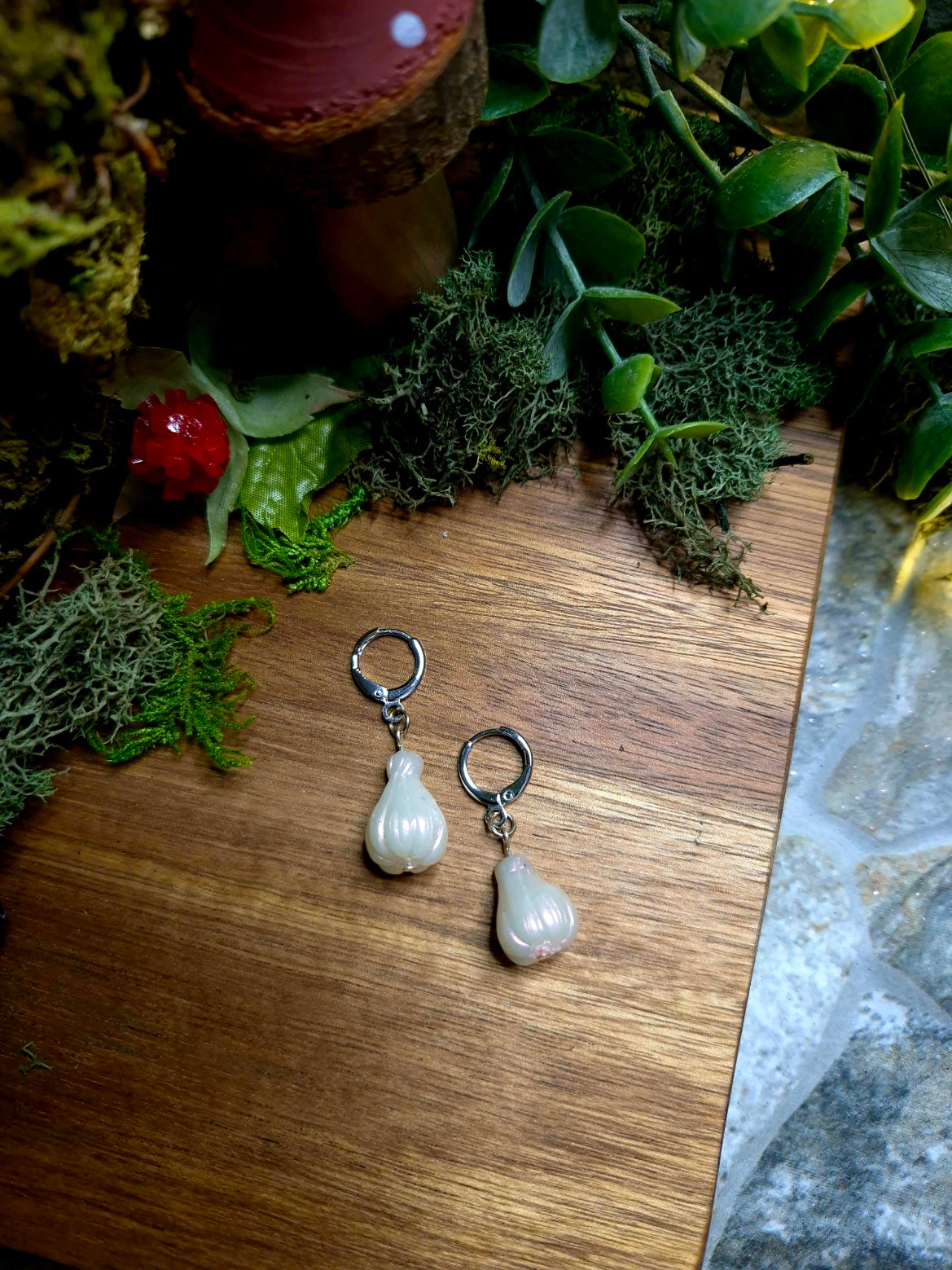 Garlic bulb earring on a wood and stone background surrounded by foliage.