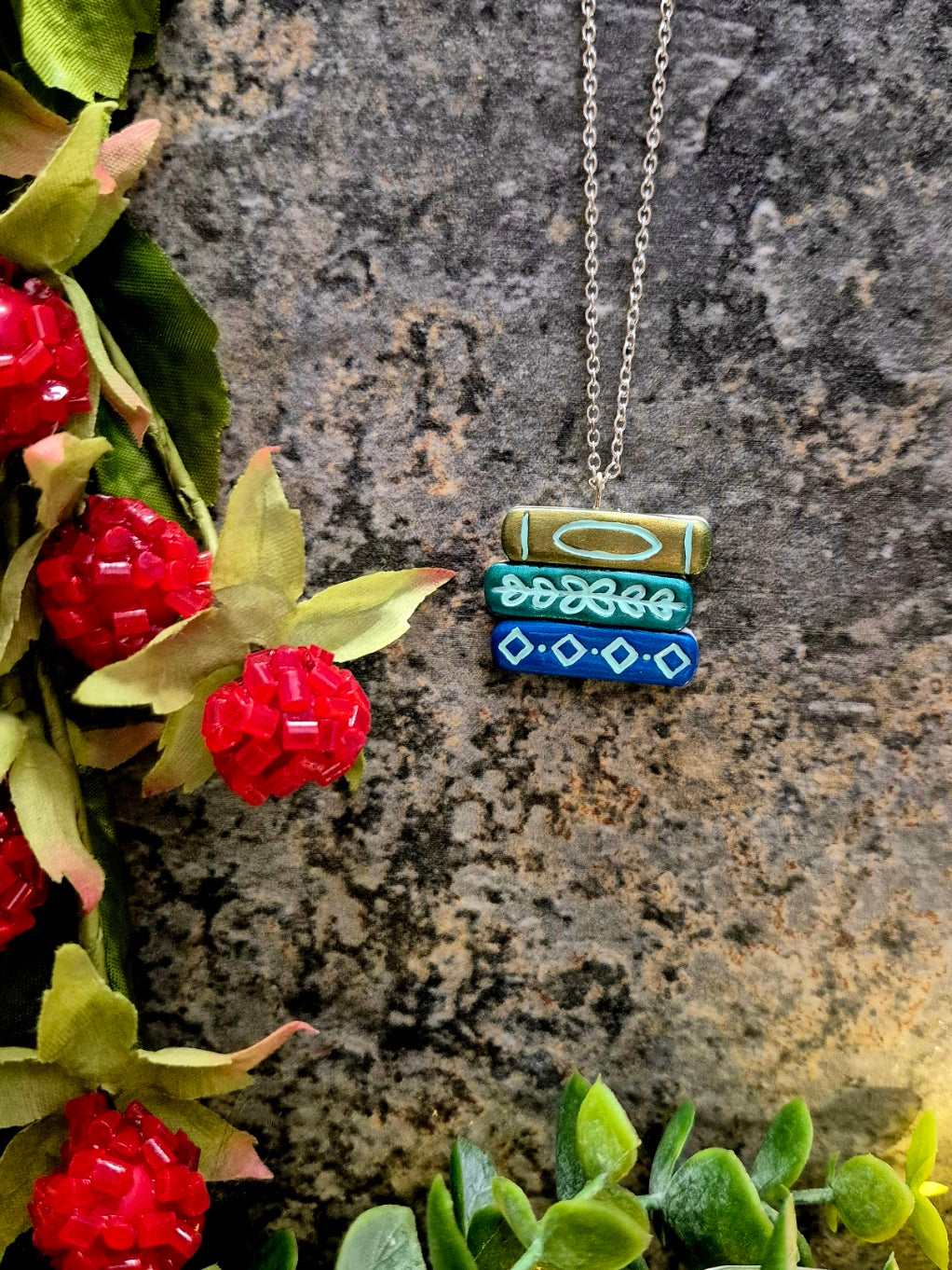 green ombre bookstack necklace on a stone background surrounded by foliage