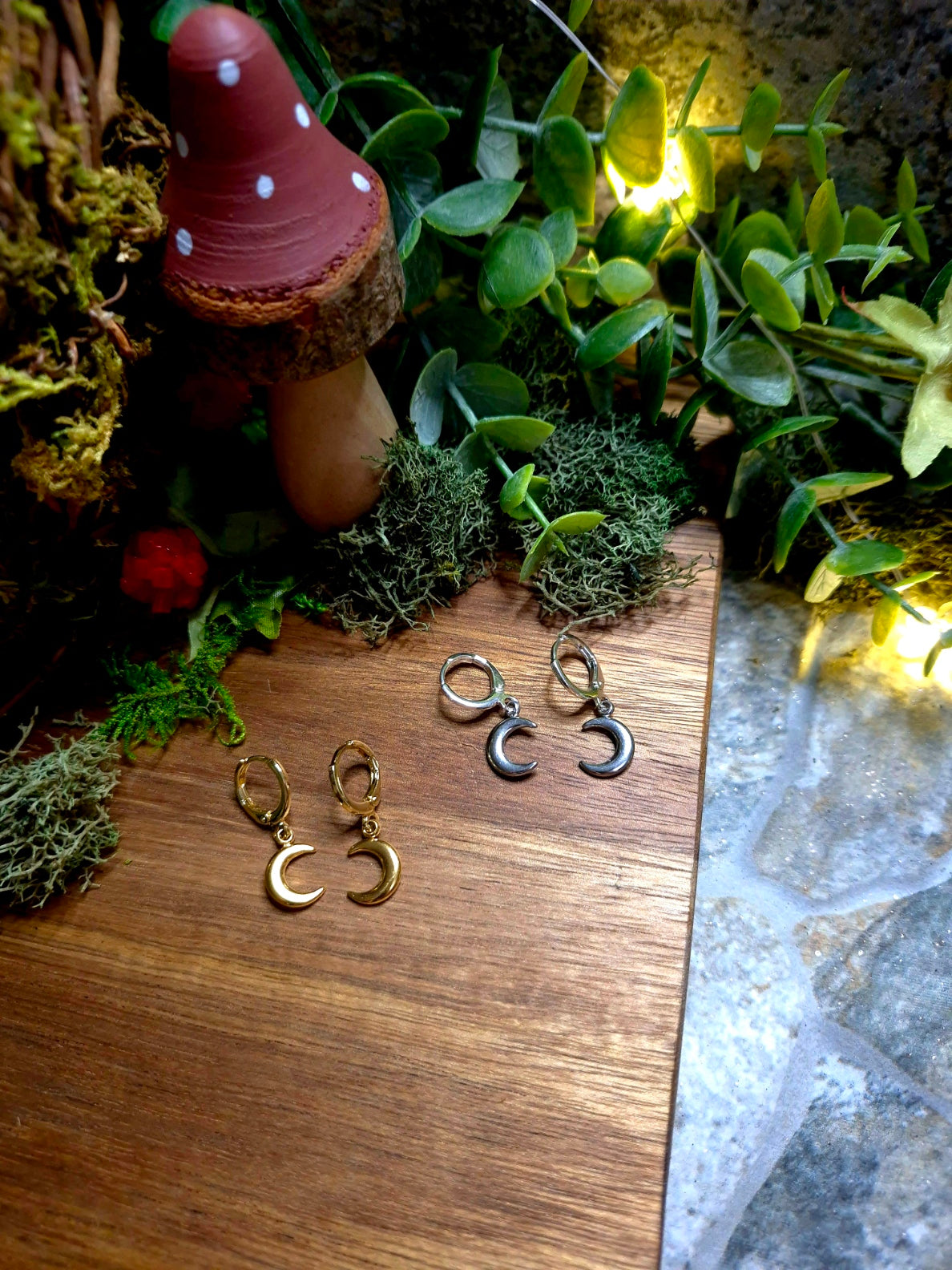 gold and silver moon charm earrings on wood and stone background