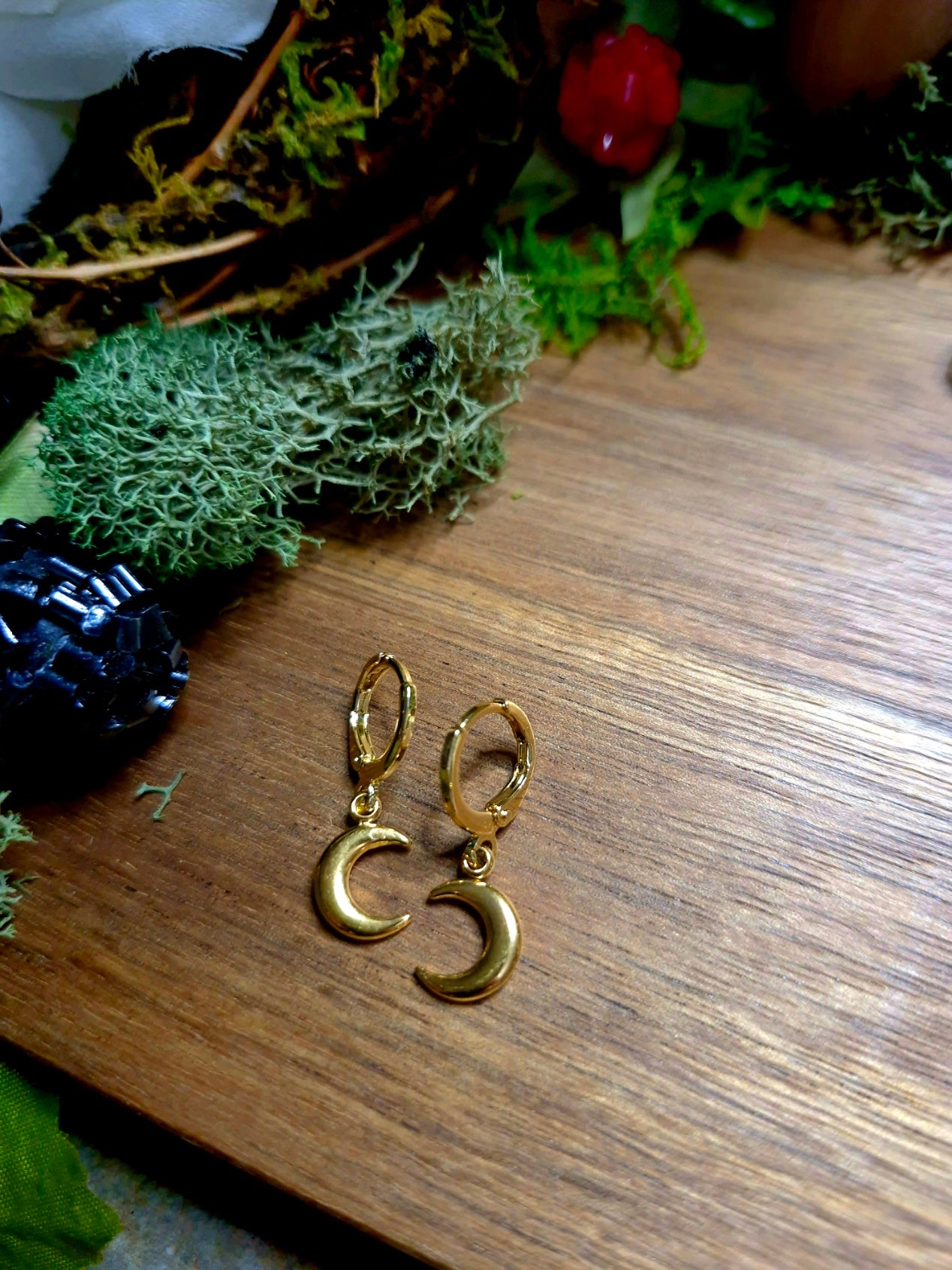 gold moon charm earrings on wood and stone background