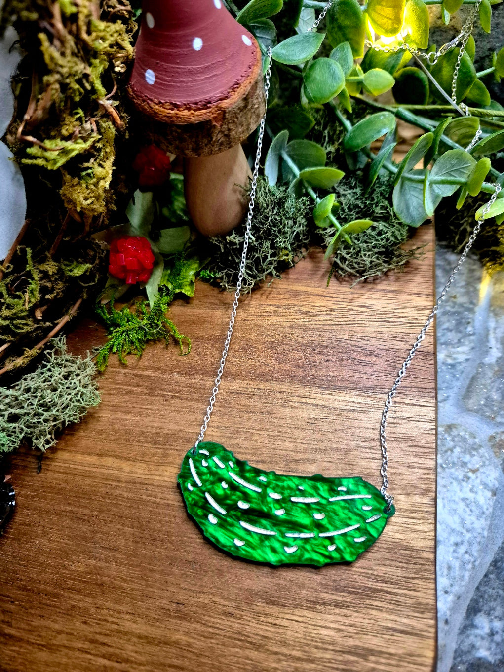 Green pickle necklace on a wood and stone background surrounded by foliage.