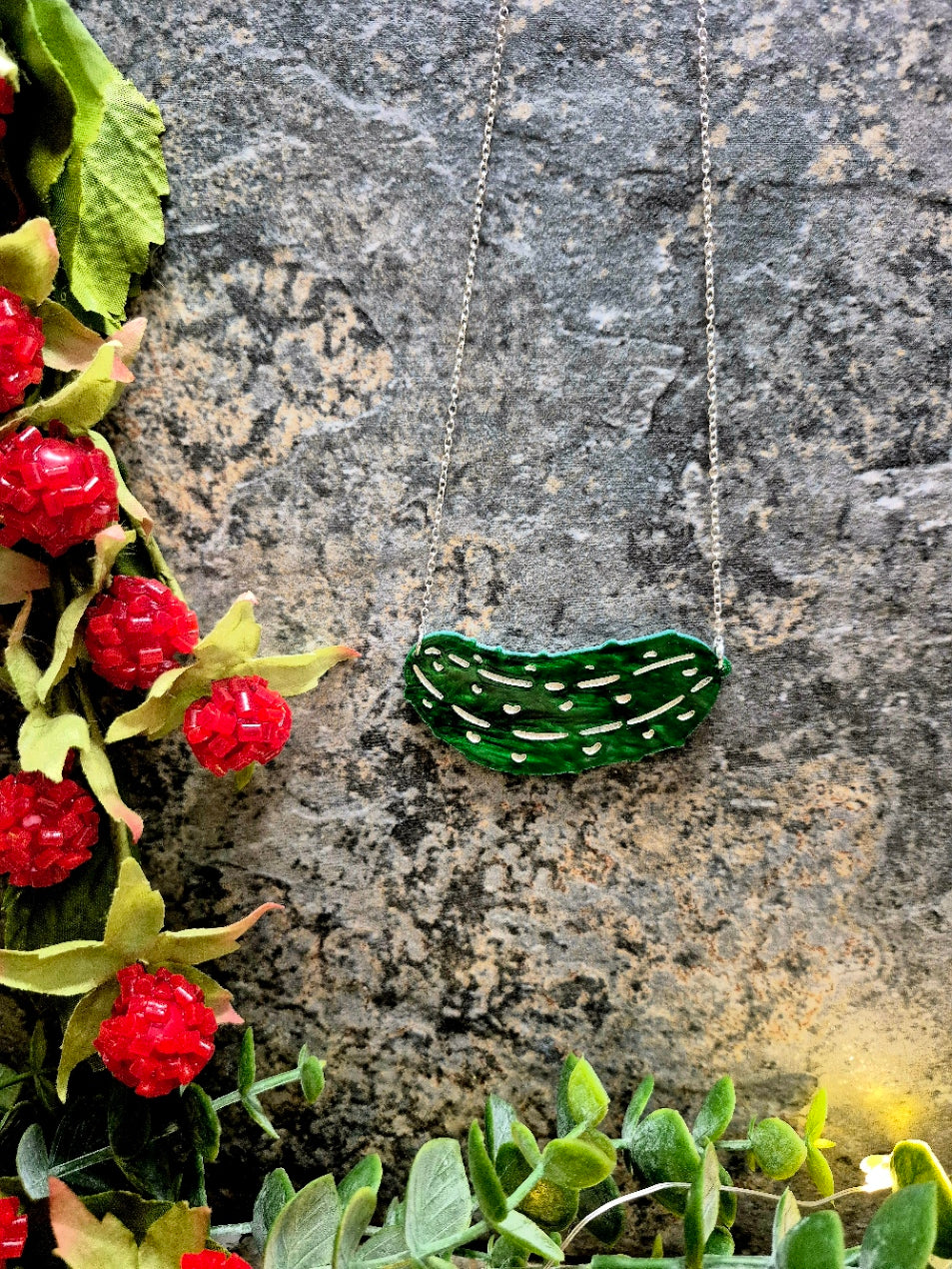 Green pickle necklace on a stone background surrounded by foliage.
