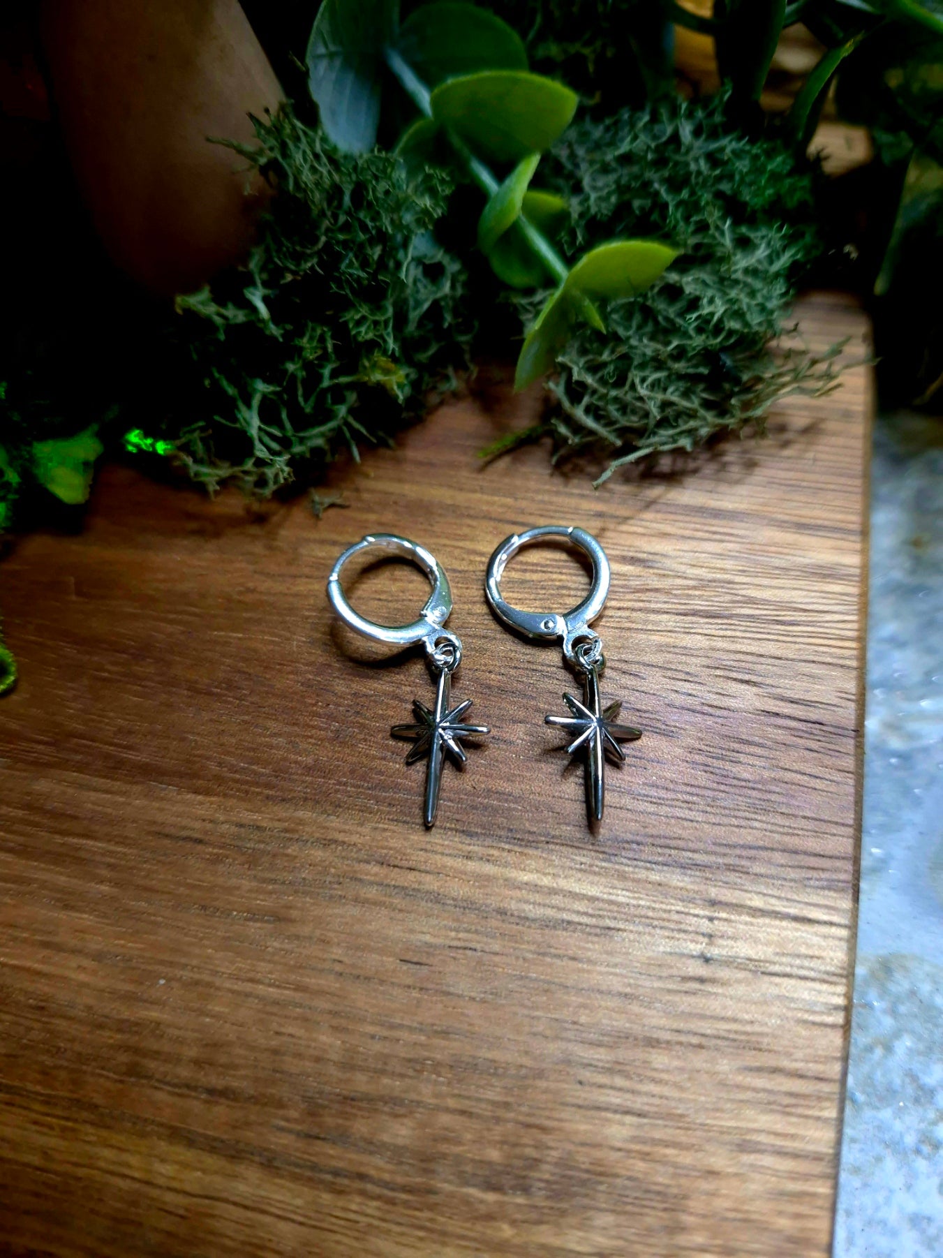 silver star earrings on a wood and stone background surrounded by foliage.