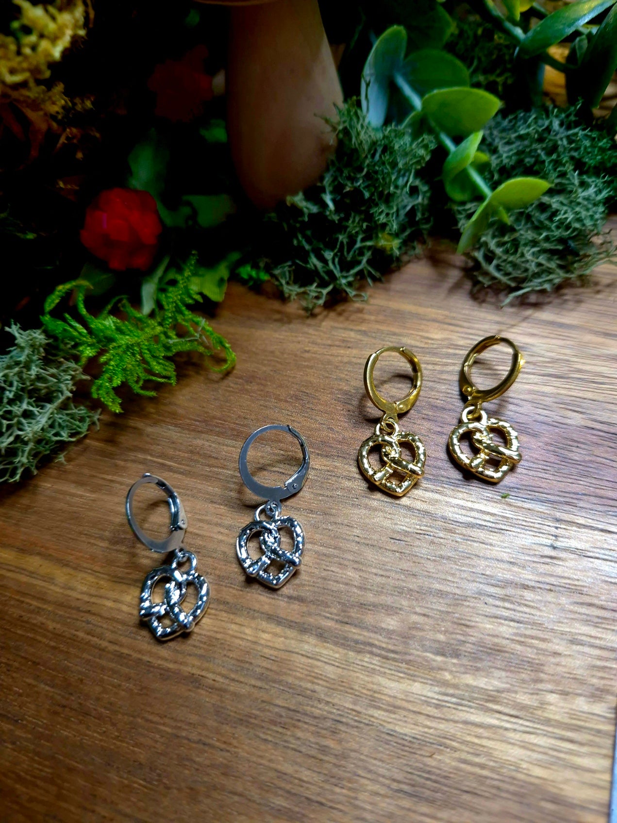 silver and gold pretzel earrings on a wood and stone background surrounded by foliage.