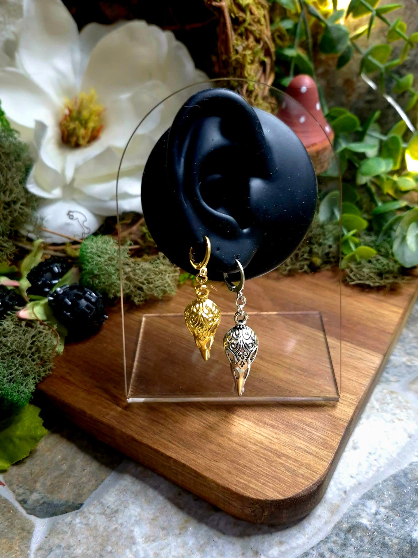silver and gold raven skull earrings on a display ear